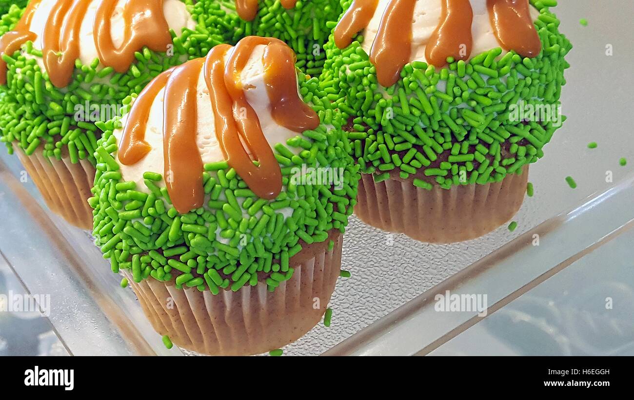 grünen Streuseln und Karamell Nieselregen auf Cupcakes Bäckerei Regal Stockfoto