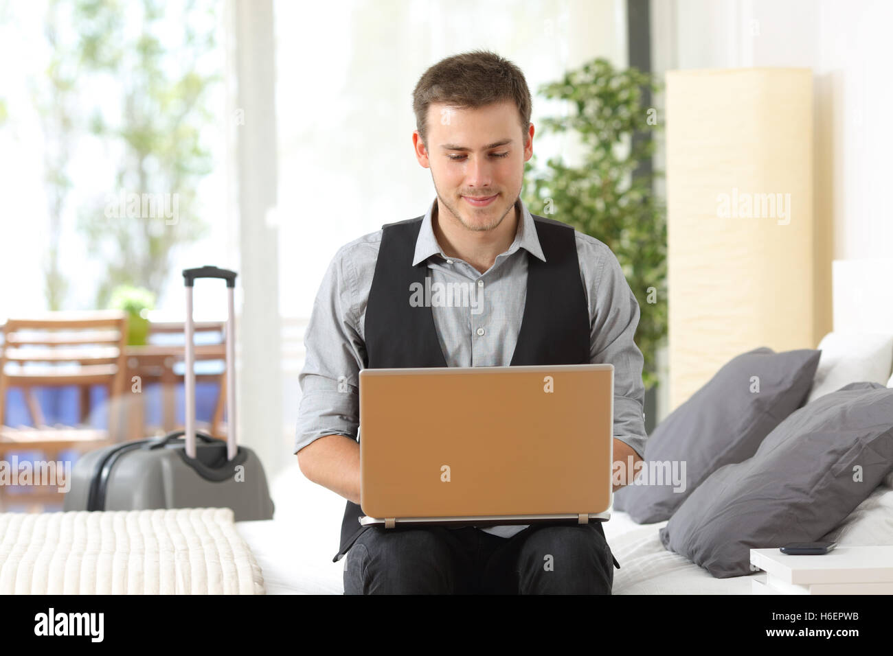 Vorderansicht Porträt eines Geschäftsmannes arbeiten auf Linie mit einem Laptop sitzt in einem Bett eines Hotelzimmers während einer Geschäftsreise Stockfoto