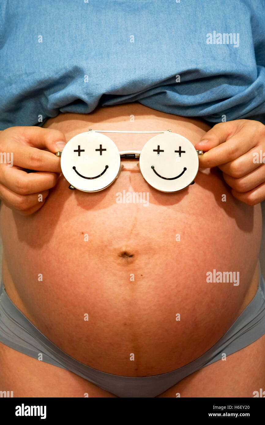 Bauch der eine junge schwangere Frau mit einen Smiley Brillen drauf Stockfoto