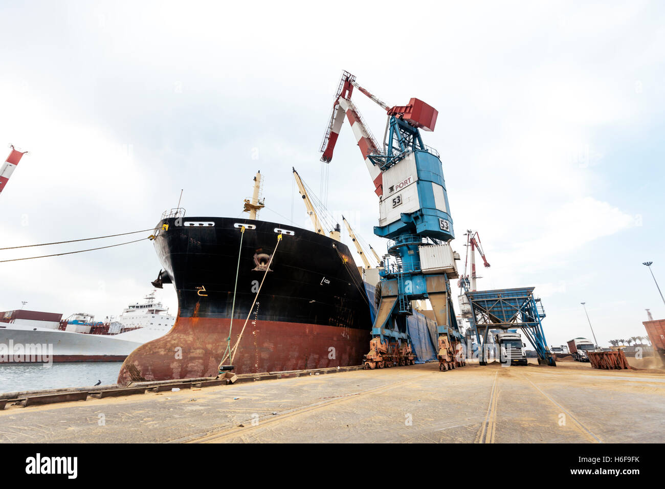 Ein Korn Frachter Schiff andocken in einem kommerziellen Hafen während ein großen Hafen Kran Gluten Sendung von ihm in einen LKW entladen wird Stockfoto