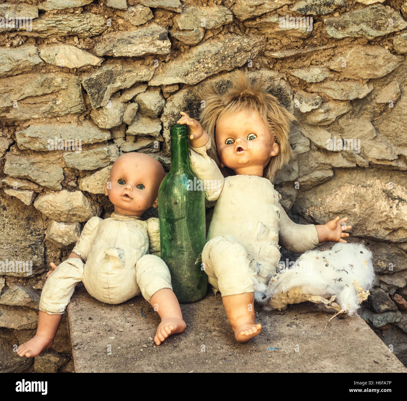 Zwei alte Puppen gegen leere Weinflasche in verlassenen Berghaus gestützt. Stockfoto