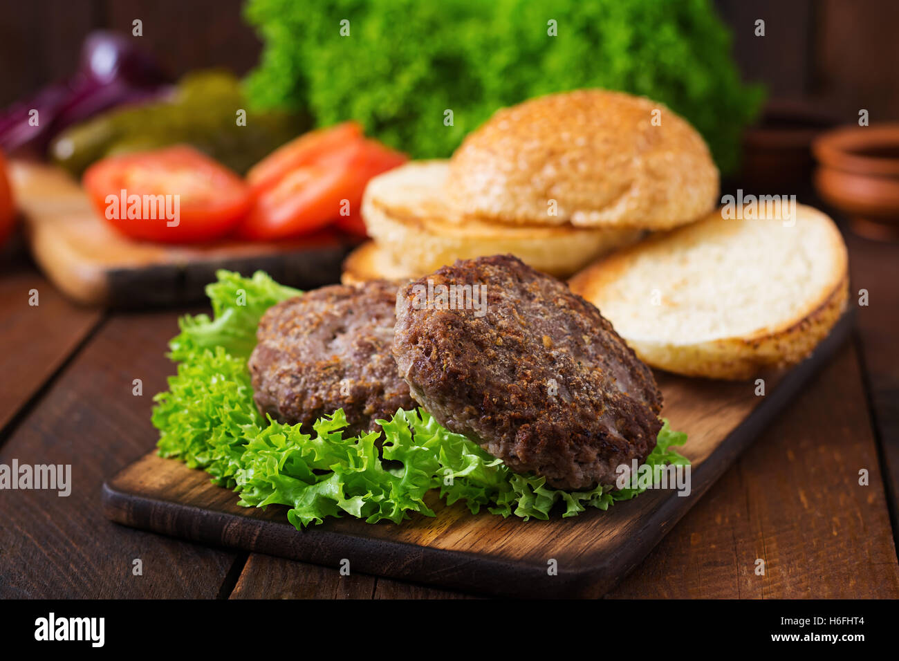 Zutaten für ein Sandwich - Hamburger Burger mit Rindfleisch, Gurken, Tomaten und roten Zwiebeln auf hölzernen Hintergrund. Stockfoto