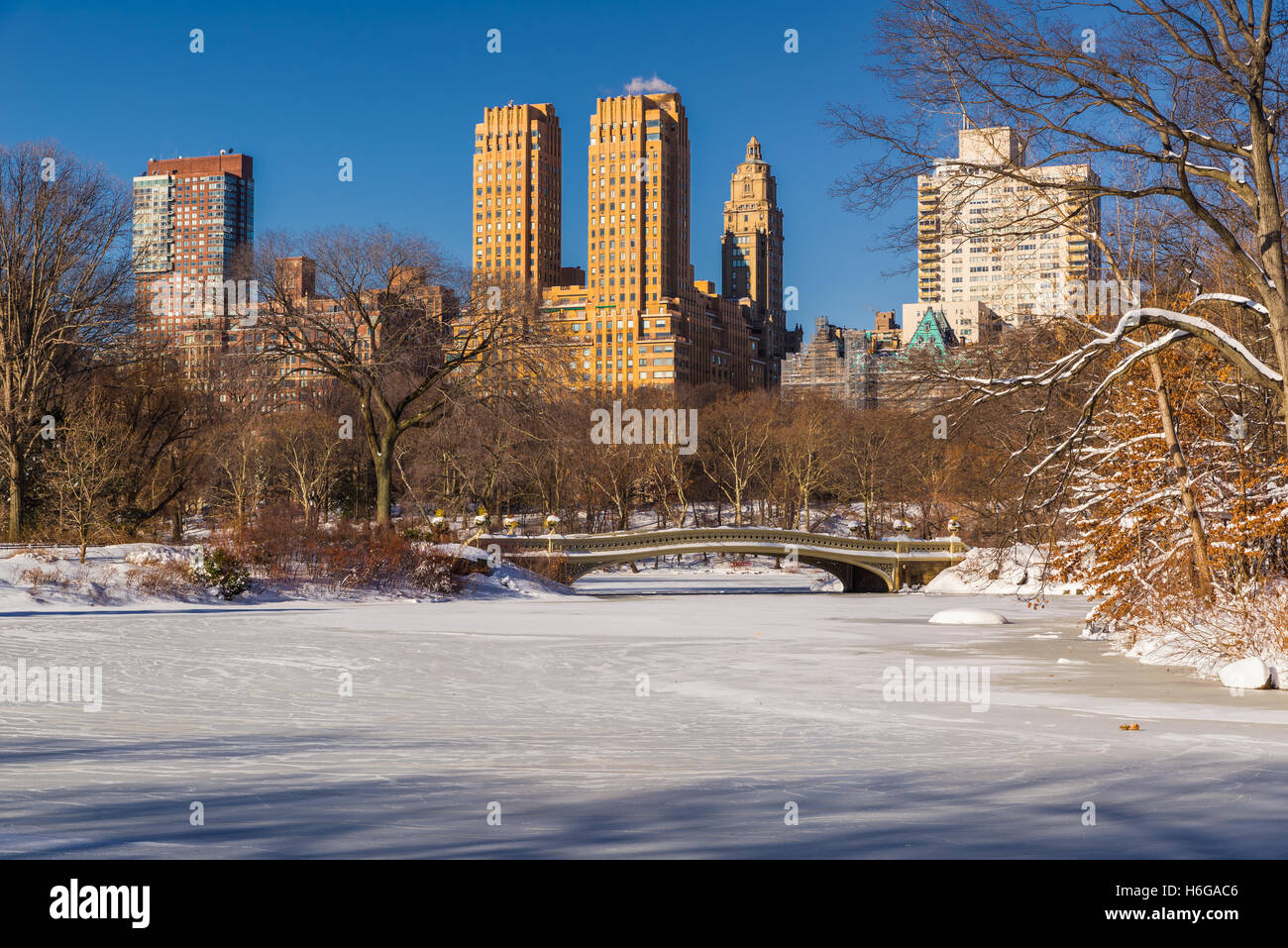 Central Park-See mit der Bogenbrücke eingefroren. Morgendliche Aussicht der Upper West Side Gebäude im Winter. Manhattan, New York City Stockfoto
