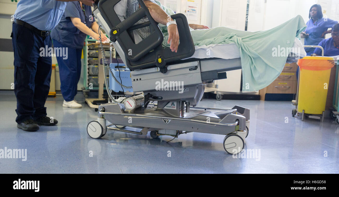 Ein Krankenhaus-Arbeiter Räder ein Patienten auf einem Wagen durch eine Station nach einer NHS-operation Stockfoto