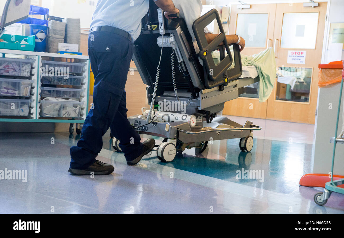 Ein Krankenhaus-Arbeiter Räder ein Patienten auf einem Wagen durch eine Station nach einer NHS-operation Stockfoto