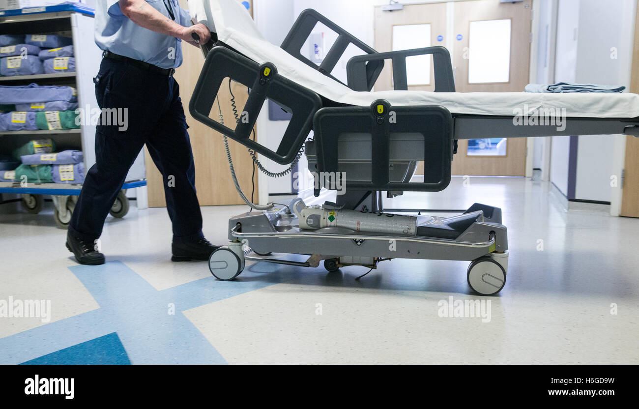 Ein Krankenhaus-Träger Räder einen leeren Wagen durch einen Korridor, ein Patient nach einer Operation NHS zu sammeln Stockfoto