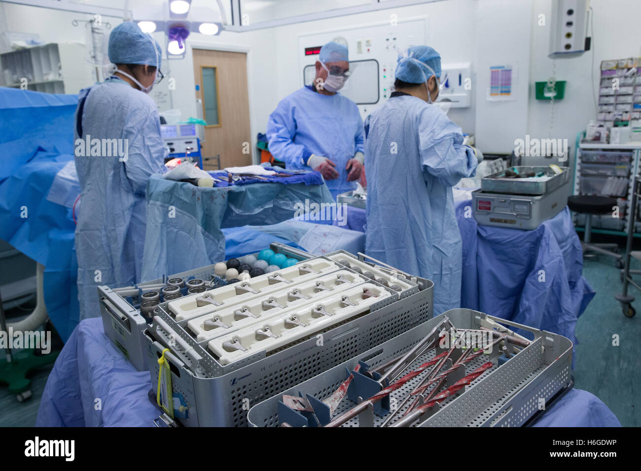 Medizinischem Personal in einem Krankenhaus-OP bei einer Knie-Ersatz-Operation. Bohrer und Ausrüstung stehen im Vordergrund. Stockfoto