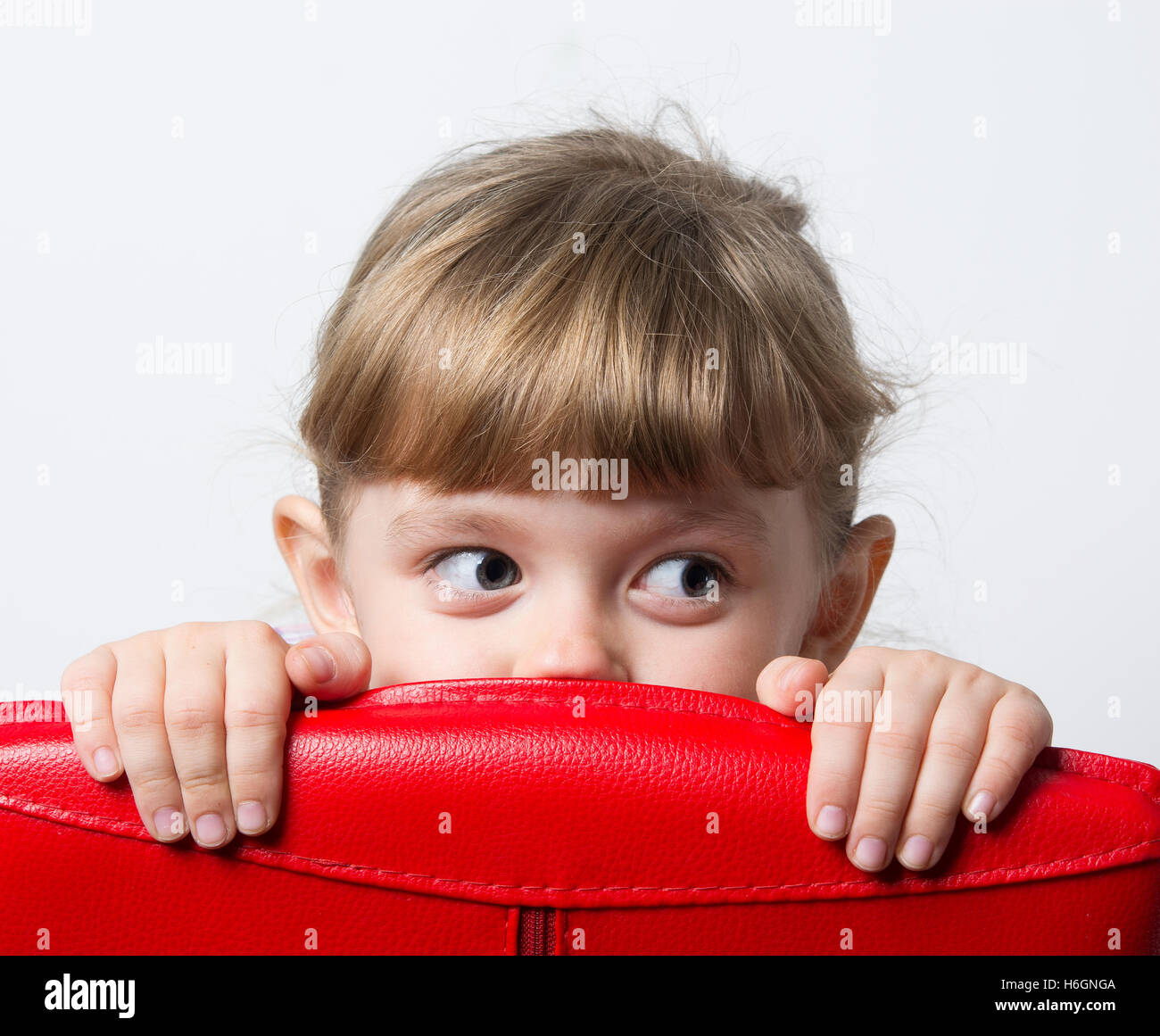 Mädchen versteckt sich hinter dem roten Stuhl Stockfoto