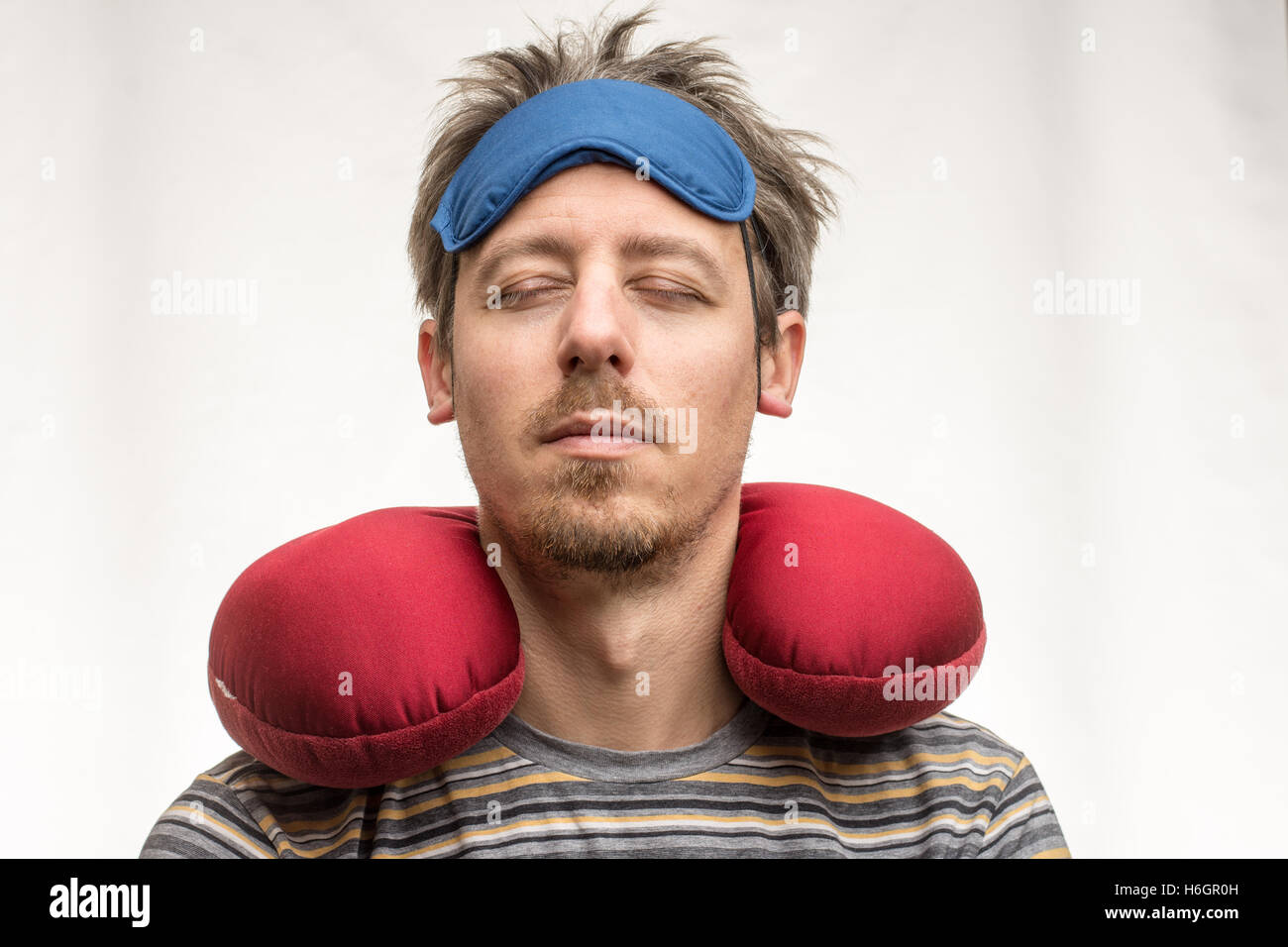 Bärtiger Mann mit Maske, rot Reisekissen und geschlossenen Augen auf weißem Hintergrund closeup Stockfoto