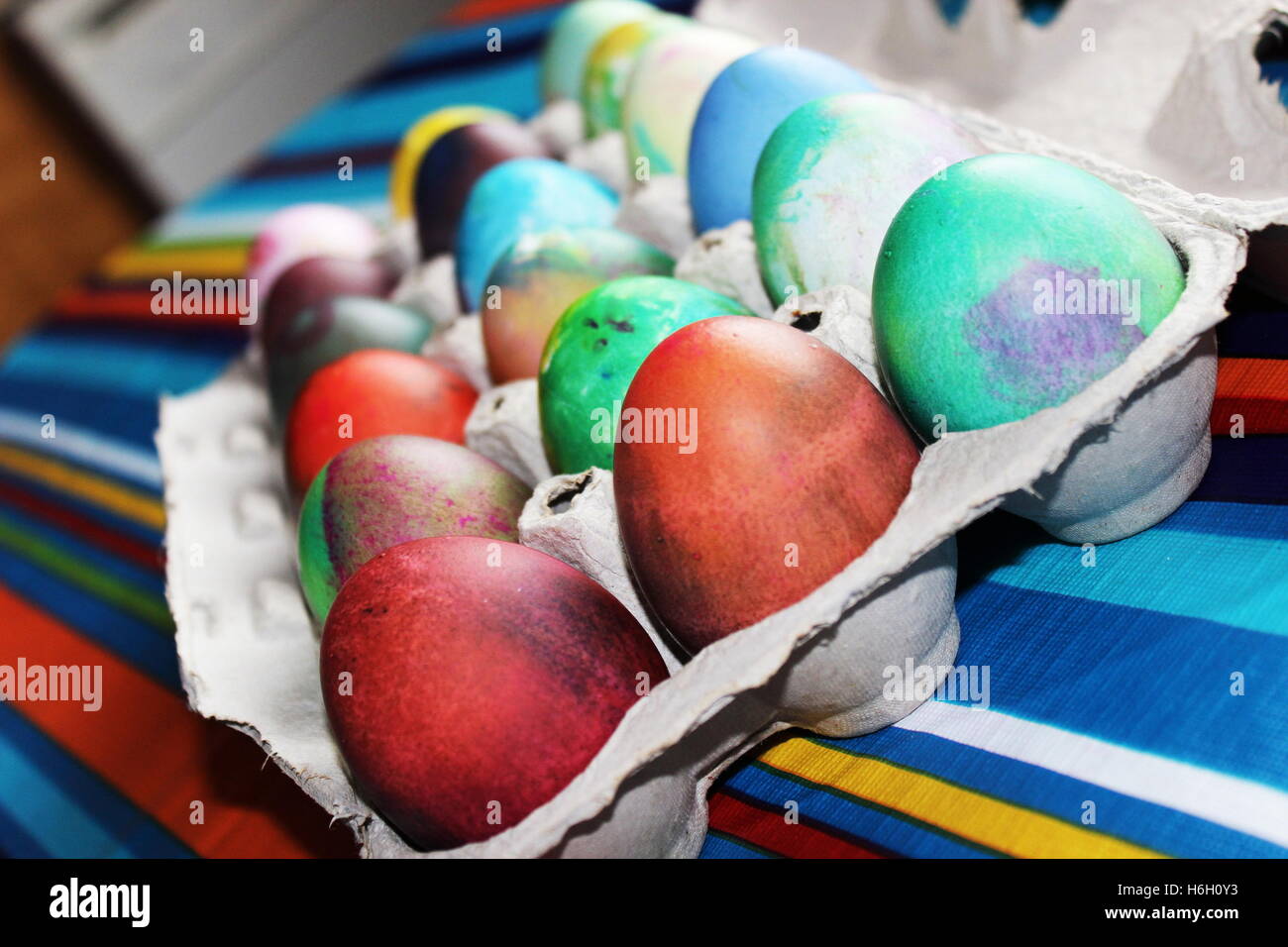 Nahaufnahme der bunt gefärbten Ostereier auf bunt gestreiften Tischdecke in ei Karton Stockfoto