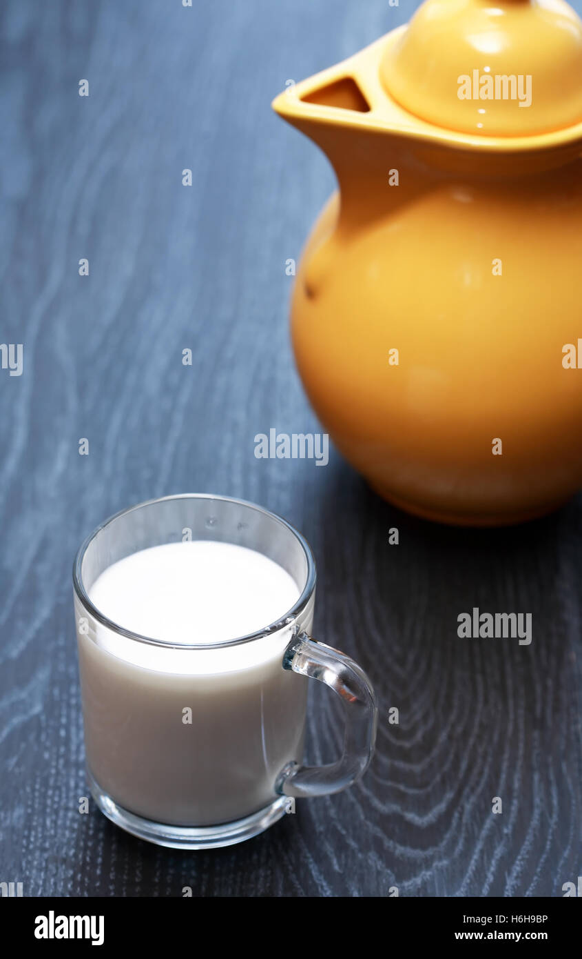 Glas voll Milch in der Nähe von gelben Krug auf dunklen Holztisch Stockfoto