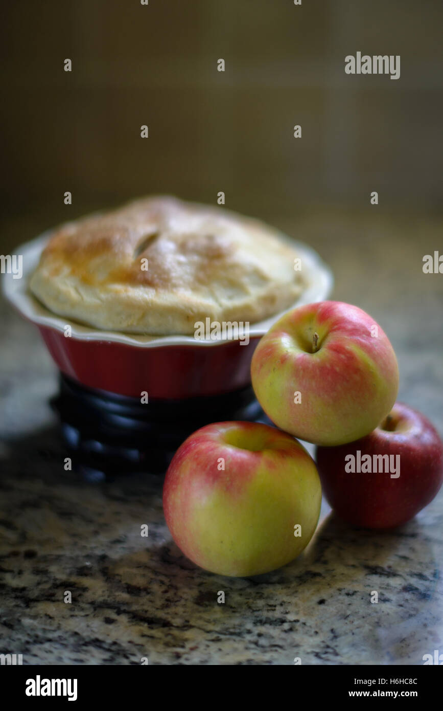 3 Äpfel vor eine kleine Torte in ein rot/Pieform Stockfoto