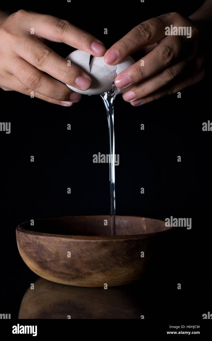 Nahaufnahme der Hände krachend Ei und Holz Schüssel auf schwarz Stockfoto