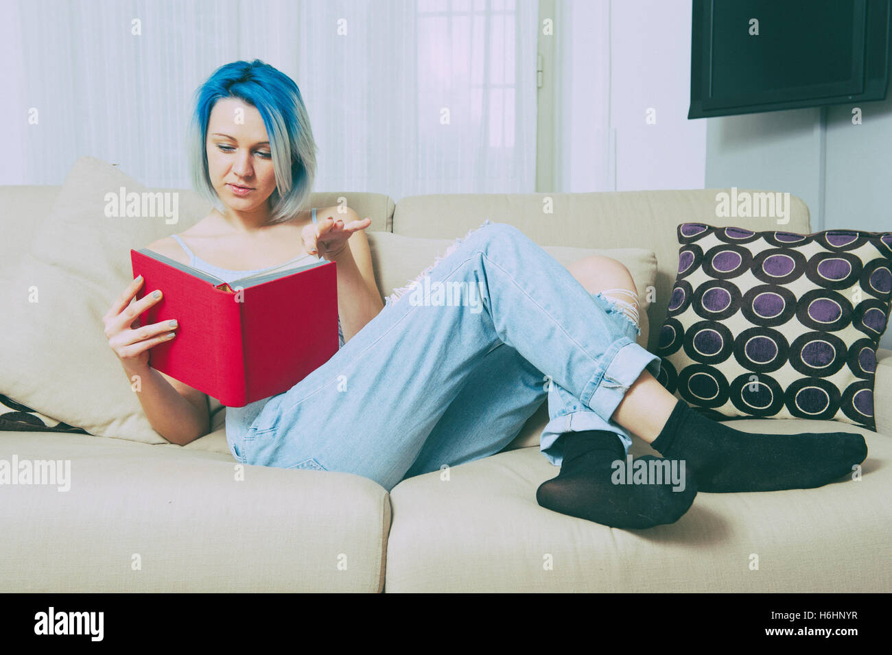Junge hübsche Teen Frau auf Sofa sitzen und rotem Einband Buch zu Hause im Wohnzimmer, Vintage Farbeffekt Stockfoto