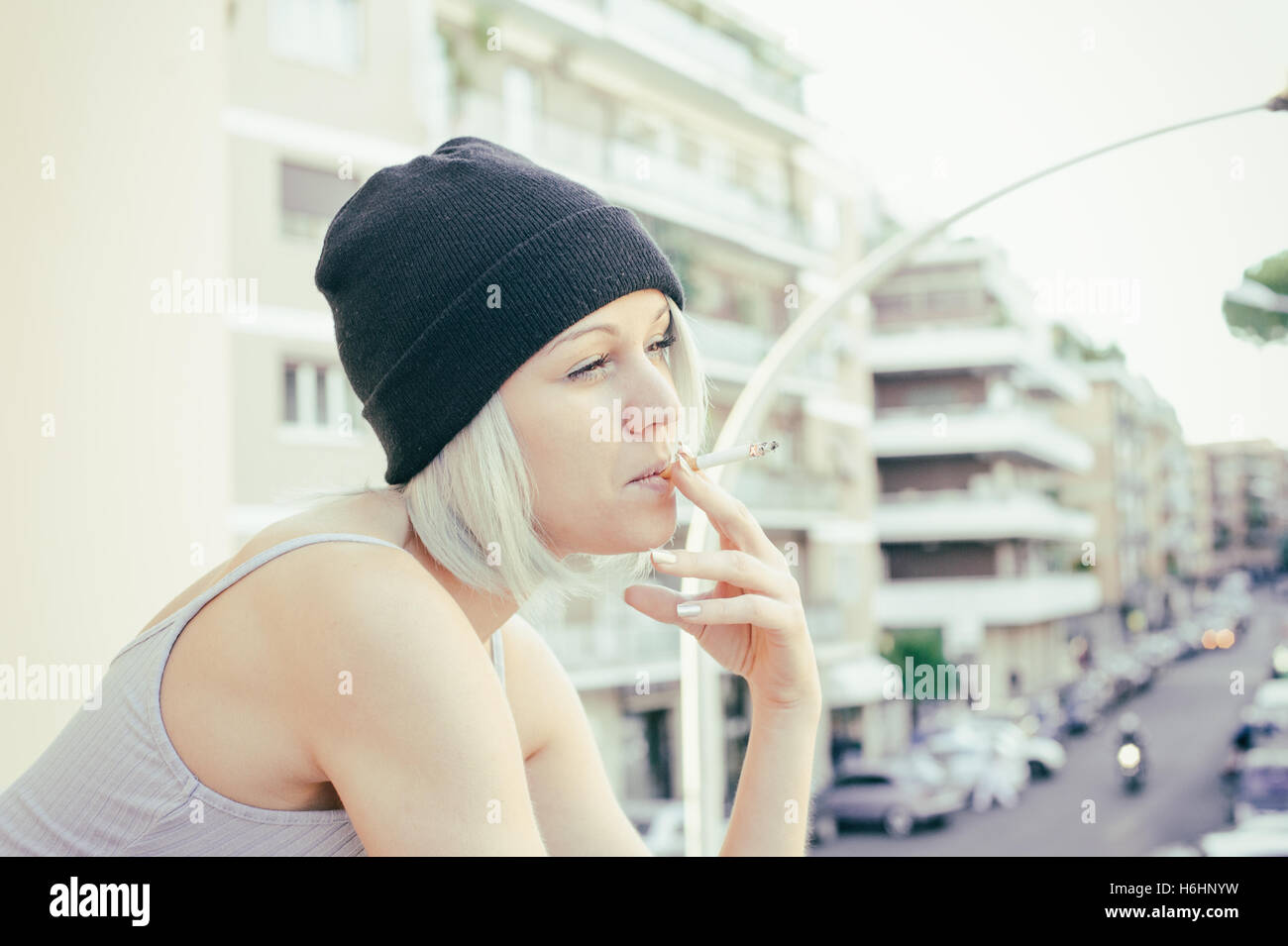 Junge Teen Frau rauchen Zigaretten und lächelnd mit urbanen Straßenbild im Hintergrund, Vintage Farbwirkung im freien Stockfoto