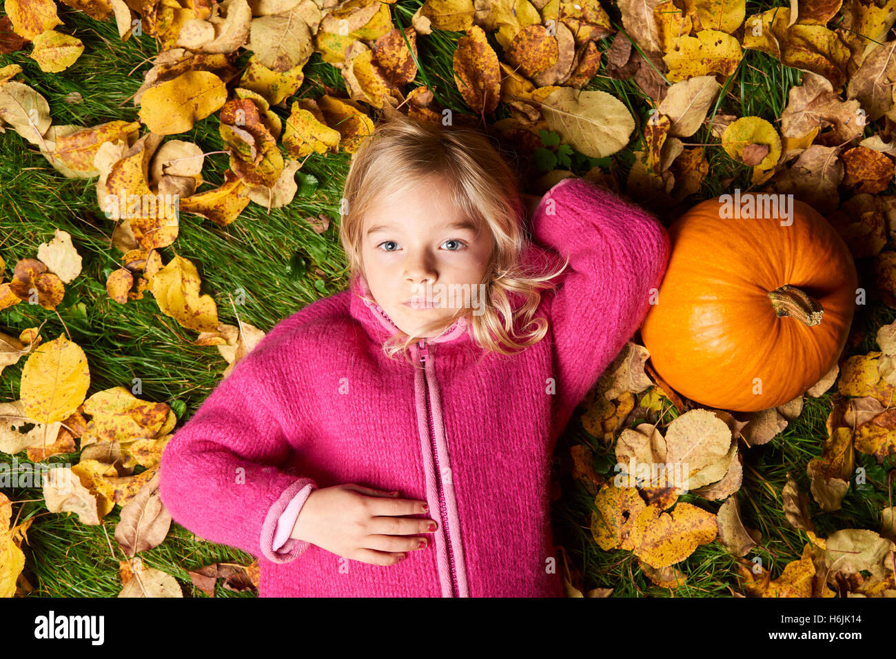 Kind süße blonde Mädchen liegen im Herbst Blätter mit Kürbis. Stockfoto