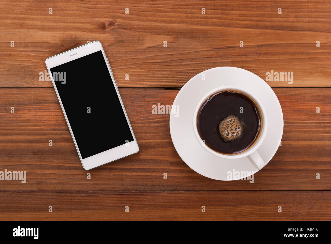 Tasse Kaffee und Handy auf einem hölzernen Hintergrund. Ansicht von oben. Stockfoto