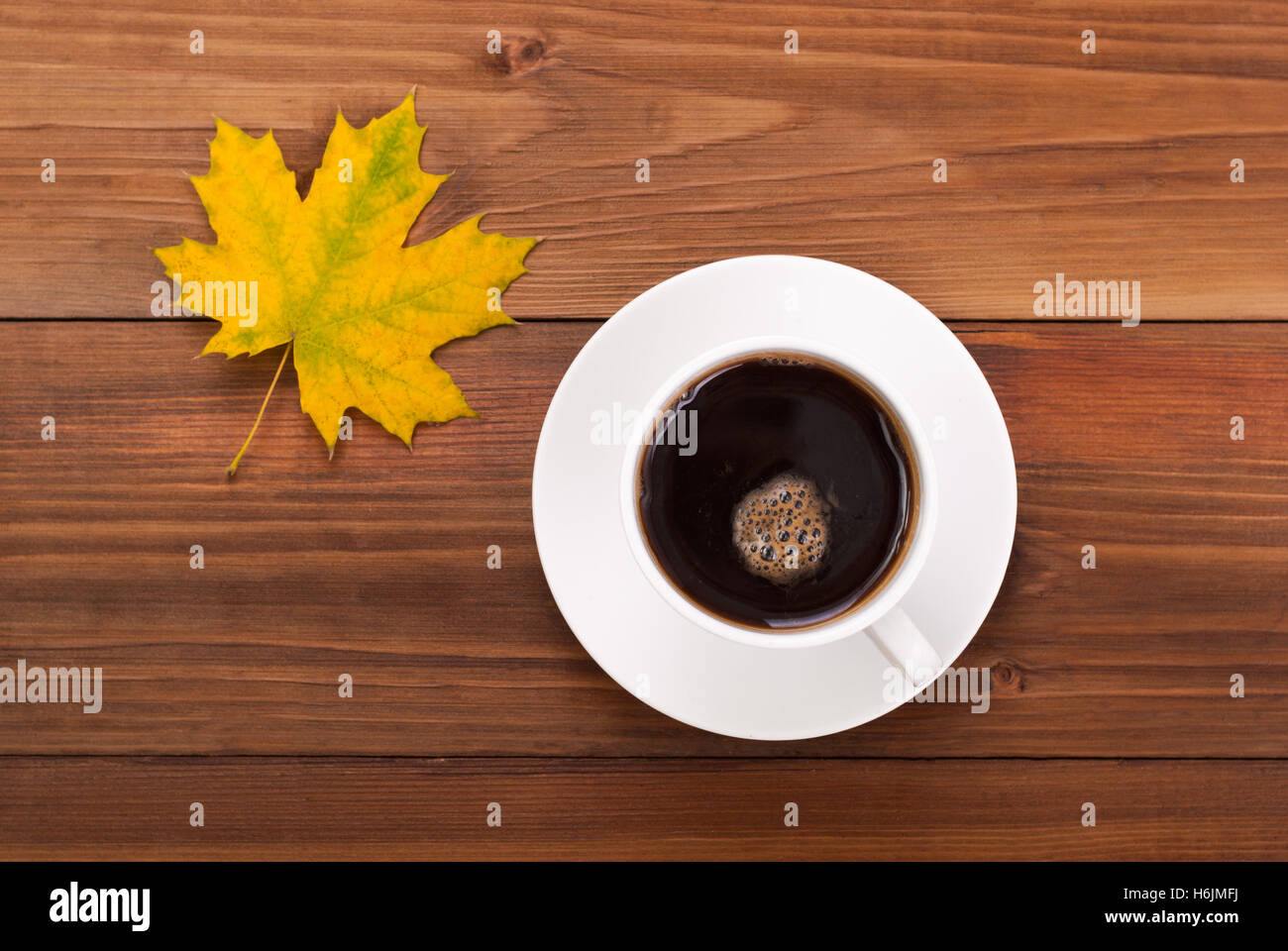 Tasse Kaffee und gelbe Ahornblatt auf einem hölzernen Hintergrund. Stockfoto