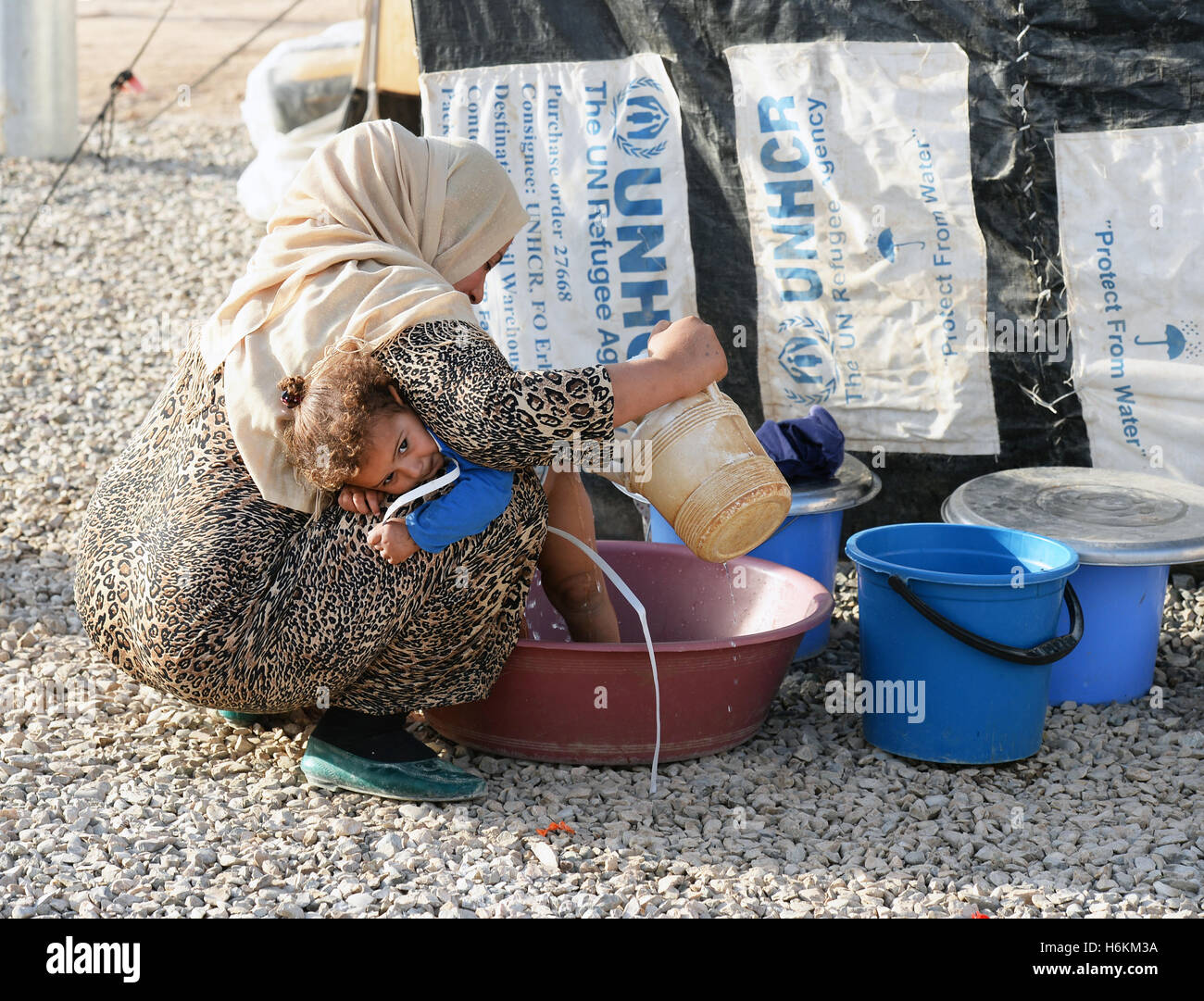 Eine Mutter wäscht ihre Tochter in einer Schüssel mit Wasser auf den staubigen Kiesweg zwischen den Unterkünften im Flüchtlingslager Debaga zwischen Mosul und Arbil, Irak, 18. Oktober 2016. Das UN-Flüchtlingshilfswerk Hilfe erwartet bis zu 1 Million Flüchtlinge aus den kämpfen um Mosul. Deutschland werden 34 Millionen Euro in Soforthilfe zur Verfügung in der Region machen. Nach Angaben von UNICEF werden mehr als 500.000 Kinder und ihre Familien große Gefahr in den nächsten Wochen durch die Rückeroberung der Stadt Mosul. Im Vorgriff auf eine Welle von Flüchtlingen sind Materialien, vor allem für die Wasserversorgung bei Stockfoto