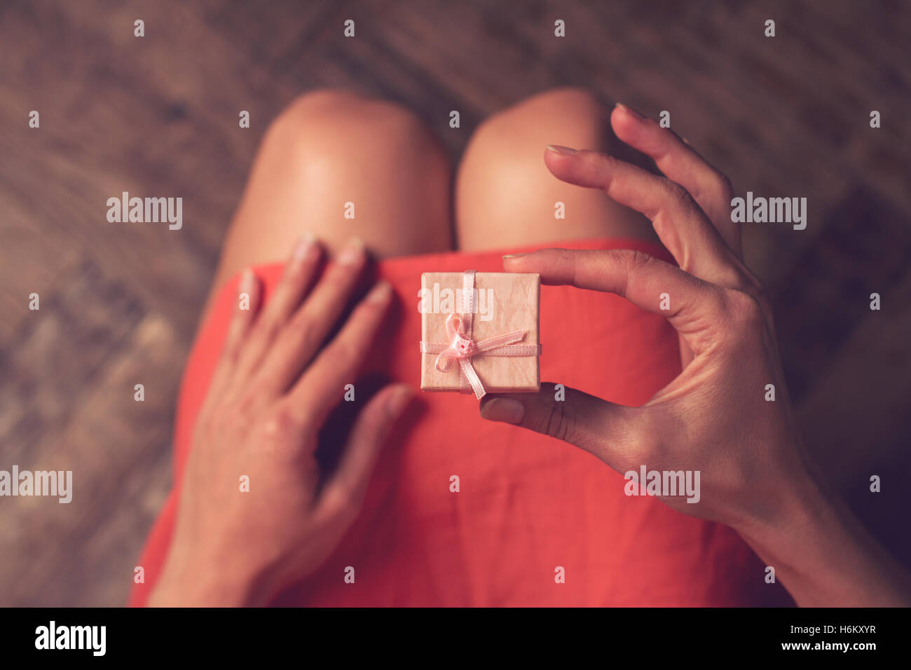Draufsicht der Frau mit rosa Kleid öffnen eine kleines Geschenkbox über die Knie Stockfoto
