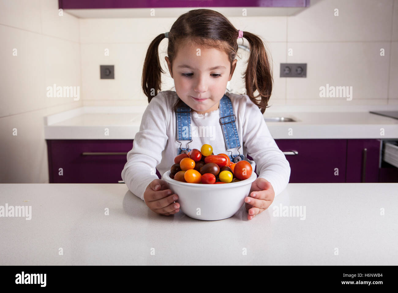 Kleines Mädchen auf der Suche einer Cherry-Tomaten-Schüssel. Aufklärung über gesunde Ernährung für Kinder Stockfoto