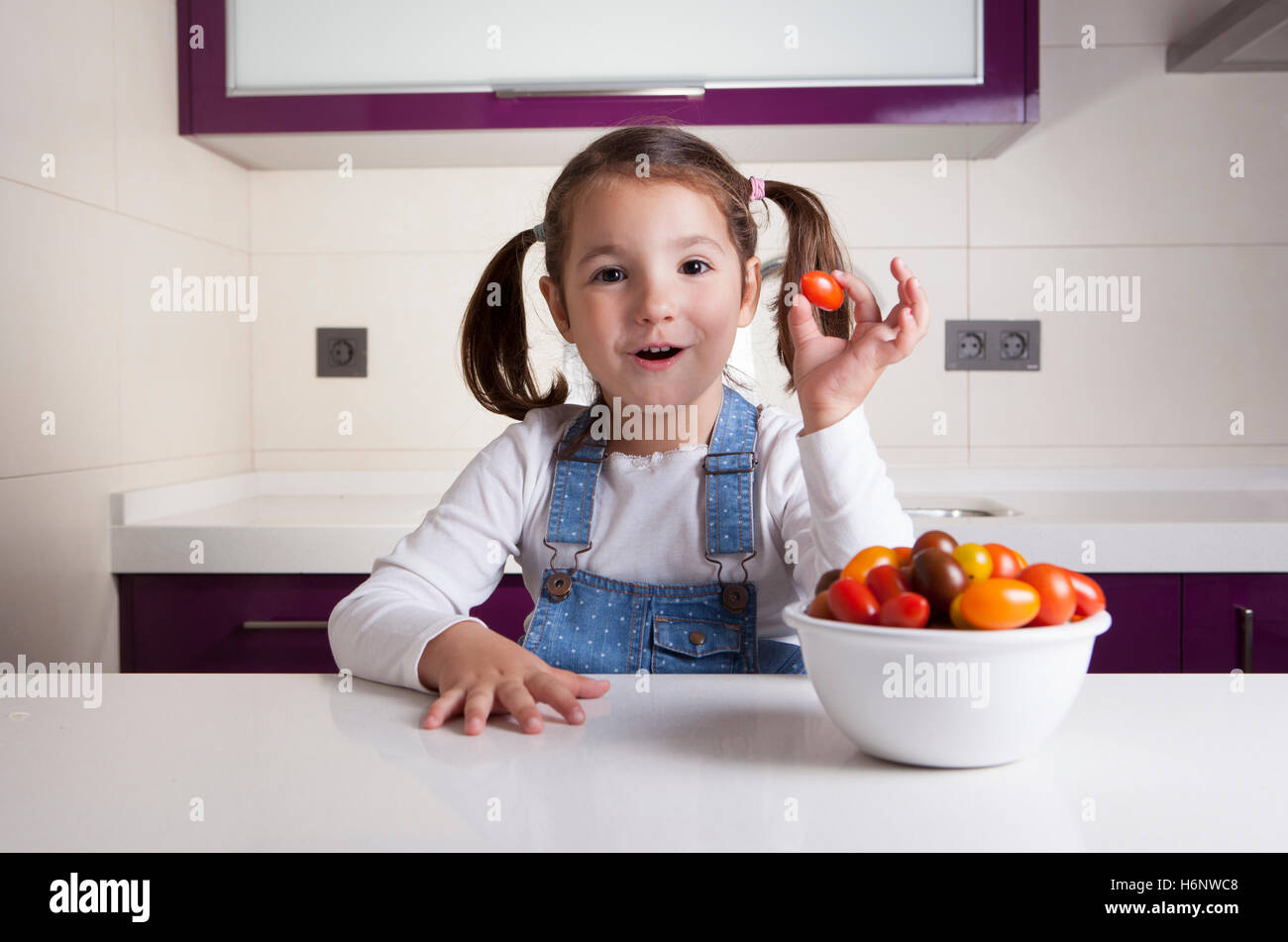 Kleines Mädchen mit Kirsche Birne Tomaten in ihrer Hand. Aufklärung über gesunde Ernährung für Kinder Stockfoto
