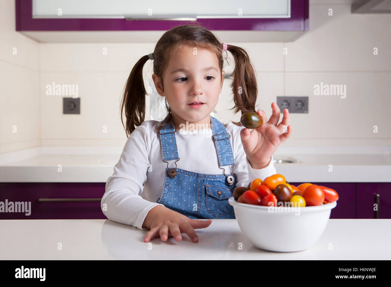 Kleines Mädchen mit Kirsche Kumato Tomaten in ihrer Hand. Aufklärung über gesunde Ernährung für Kinder Stockfoto
