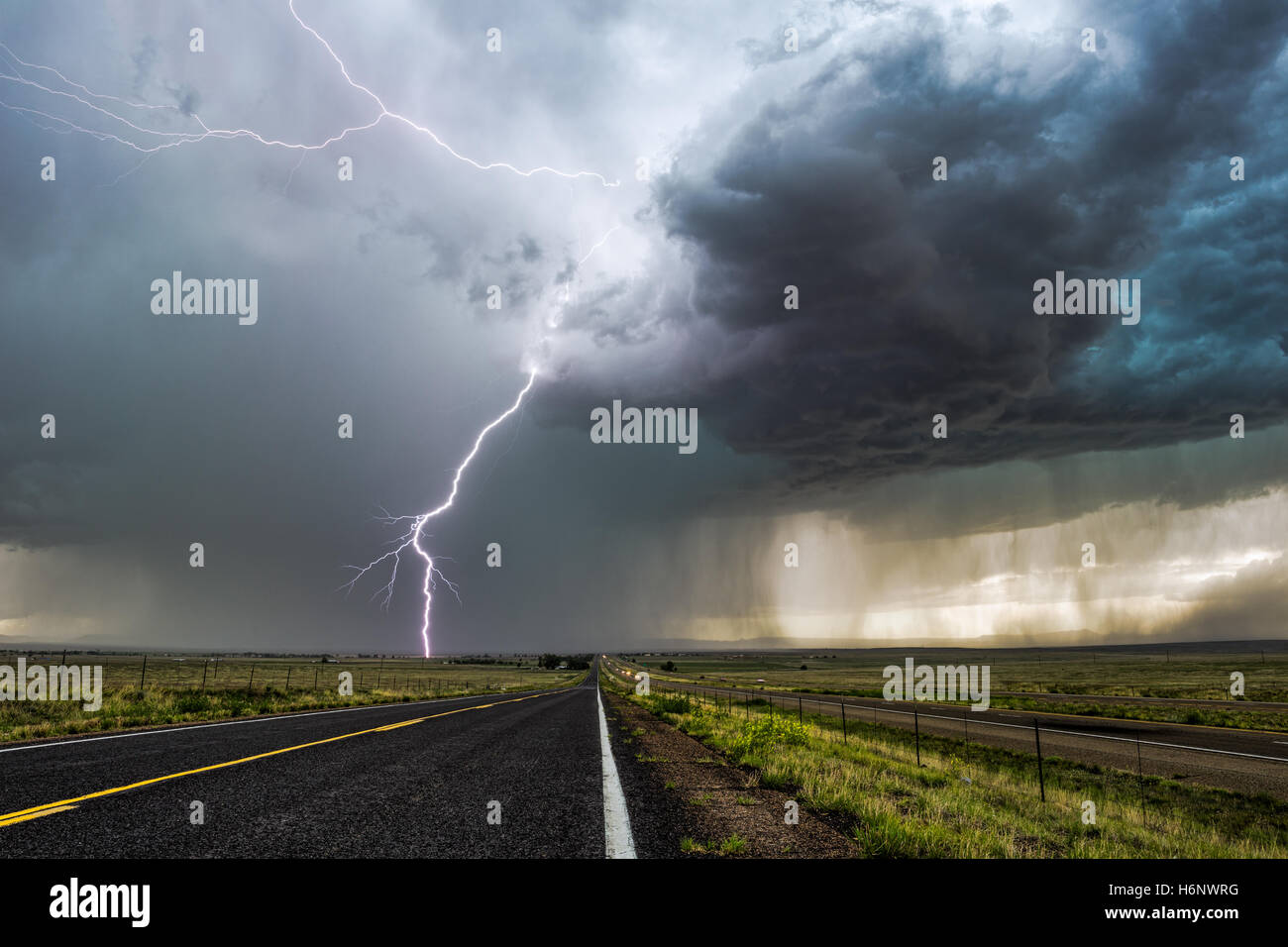 Ein heller Blitz, der während eines Sturms in der Nähe von Springer, New Mexico, über einer langen Straße einstürmt Stockfoto