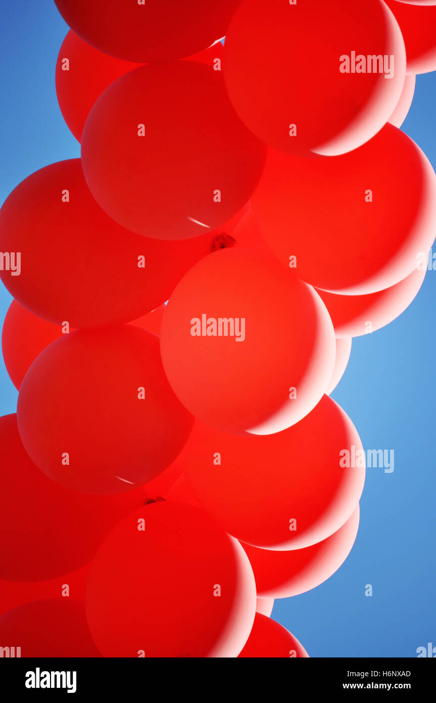 Eine Reihe von roten Ballons schweben durch die Luft an einem sonnigen Tag mit blauem Himmel. Stockfoto