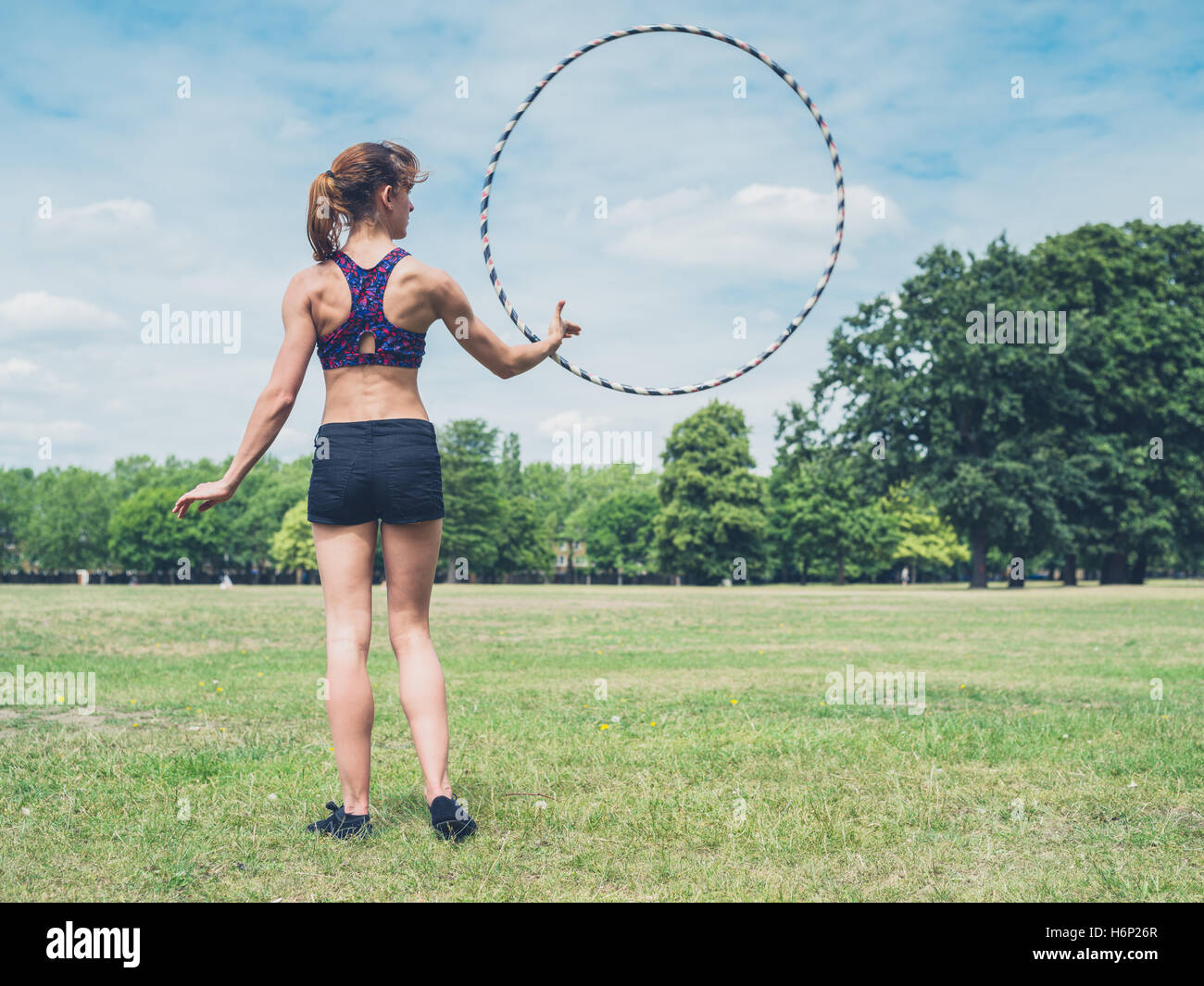 Eine Passform und sportliche junge Frau ist einen Hula Hoop Reifen im Park an einem sonnigen Sommertag drehend Stockfoto