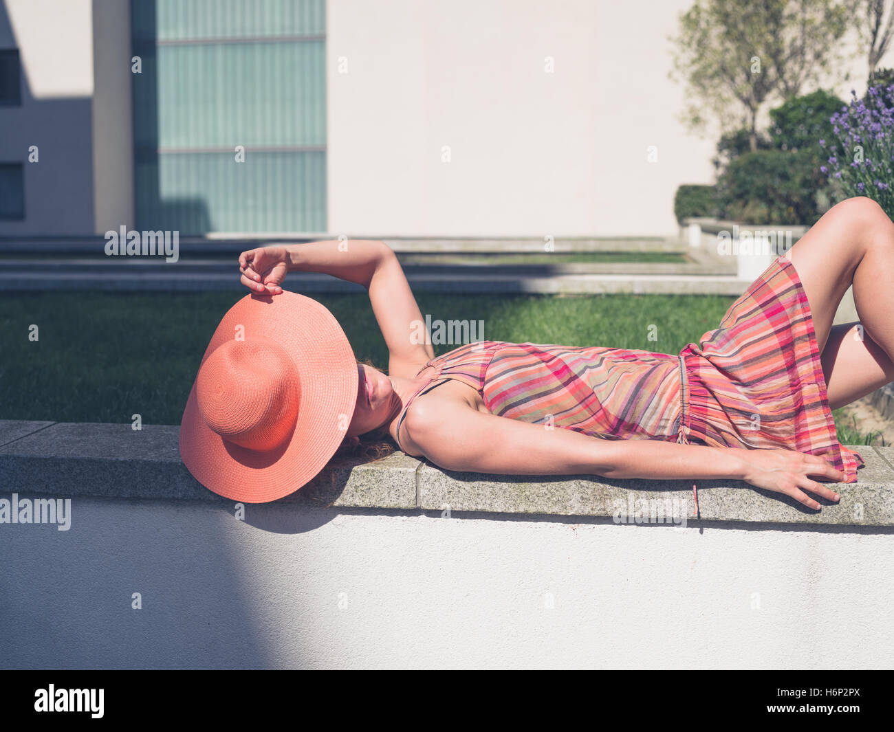 Eine junge Frau trägt ein Kleid und einen Hut ist entspannend außerhalb an einem sonnigen Sommertag Stockfoto