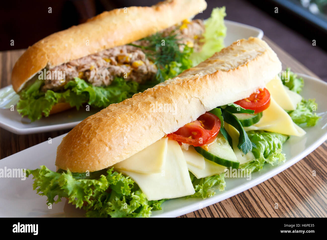 Käse und Salat Baguette auf weißen Teller. Thunfisch Baguette im Hintergrund. Stockfoto
