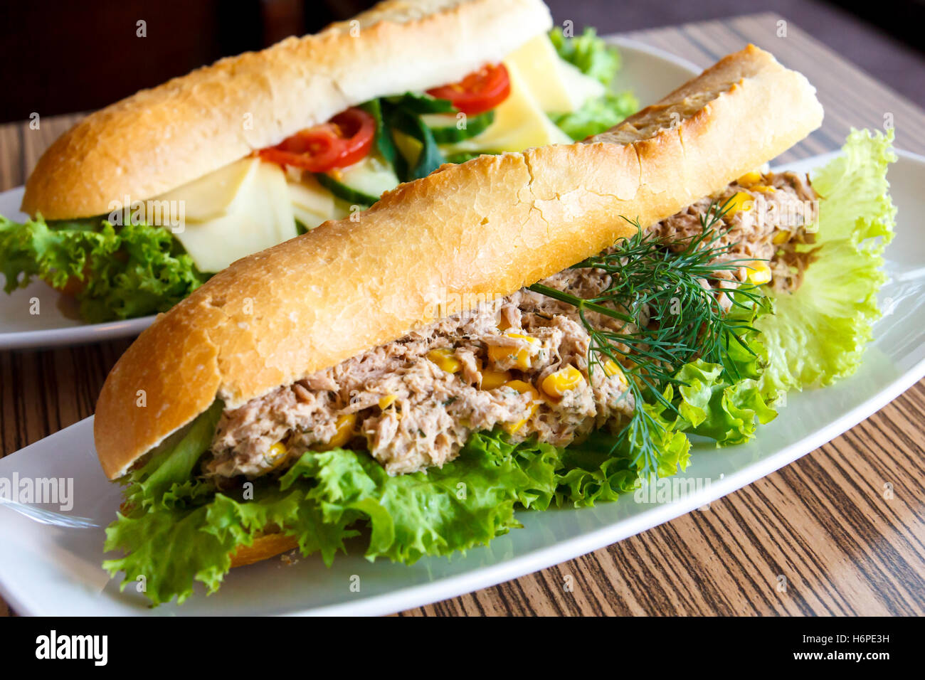 Thunfisch und Salat Baguette auf weißen Teller. Käse-Baguette im Hintergrund. Stockfoto