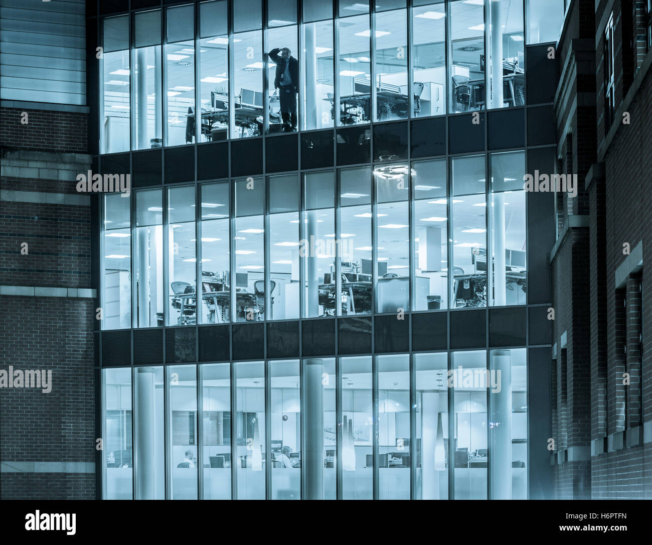 Mann allein im Büro, der nachts aus dem Fenster schaut: Energieeinsparung, Arbeit von zu Hause aus Stress, psychische Gesundheit, Einsamkeit ... Konzept. Stockfoto