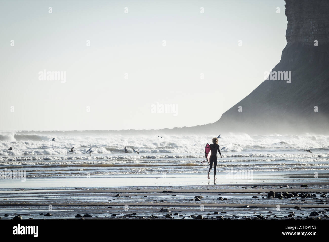 Surfer am Strand mit Surfbrett am Saltburn durch Meer, North Yorkshire, England, Vereinigtes Königreich laufen. Stockfoto