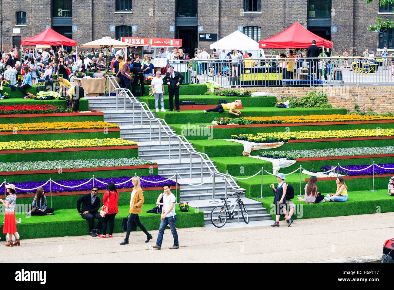 Sonnenanbeter auf die Schritte der Getreidespeicher Square von Regent's Canal in King's Cross, London, UK, geschmückt mit künstlichem Gras und Blumen, 2014 Stockfoto