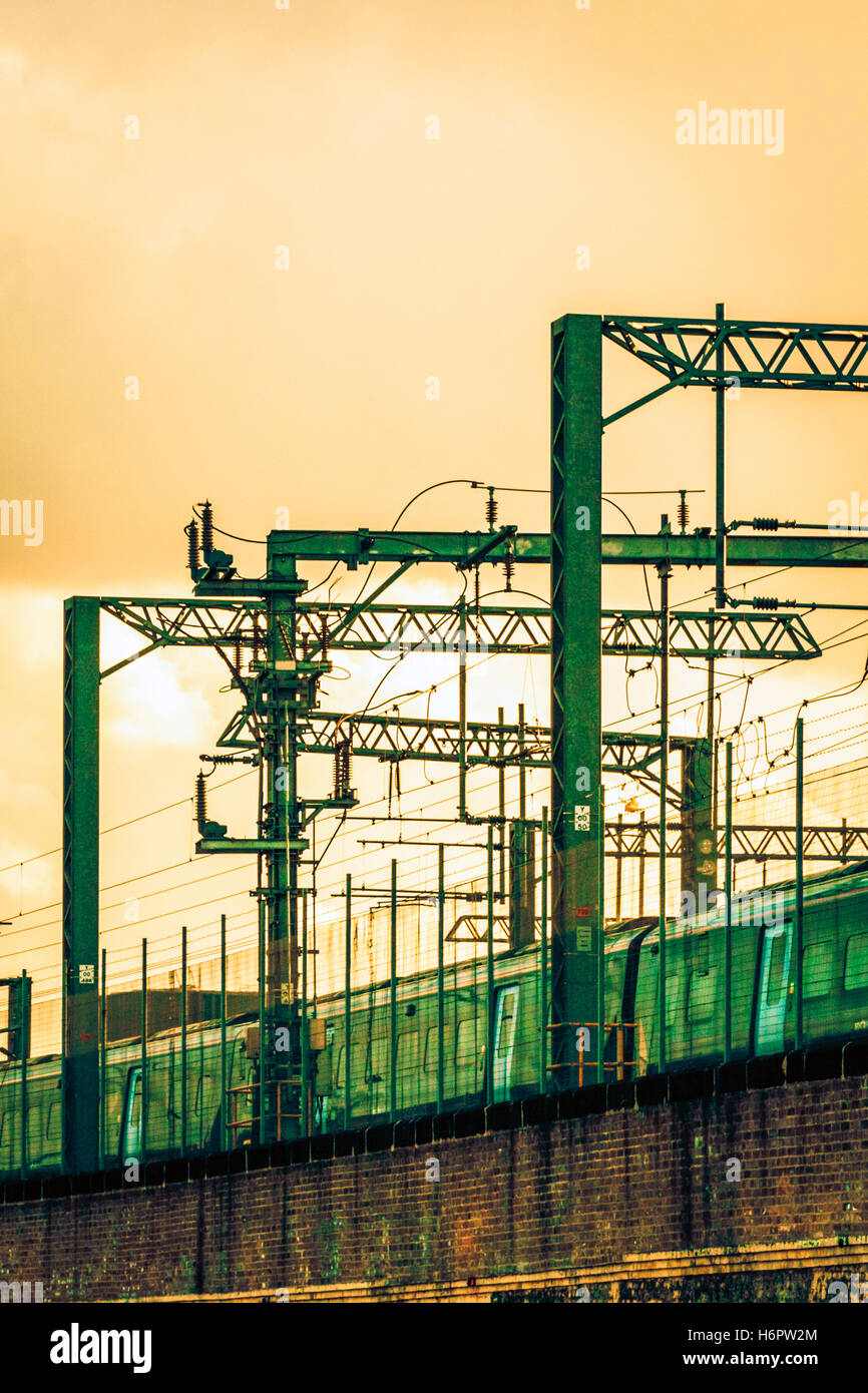 Gelb Himmel bei Sonnenuntergang über Portale und elektrischen Drähten an der Eisenbahnlinie von St. Pancras International Station, London, UK, ein Zug vorbei, 2012 Stockfoto