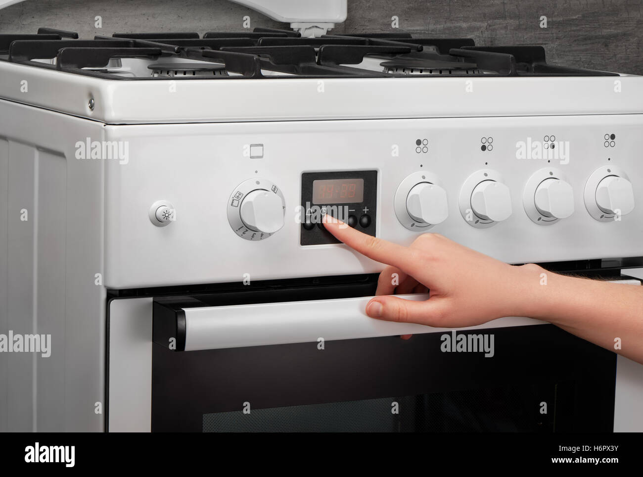 Weibliche Hand drehen auf weiße Küche Gasherd auf grauem Hintergrund Stockfoto