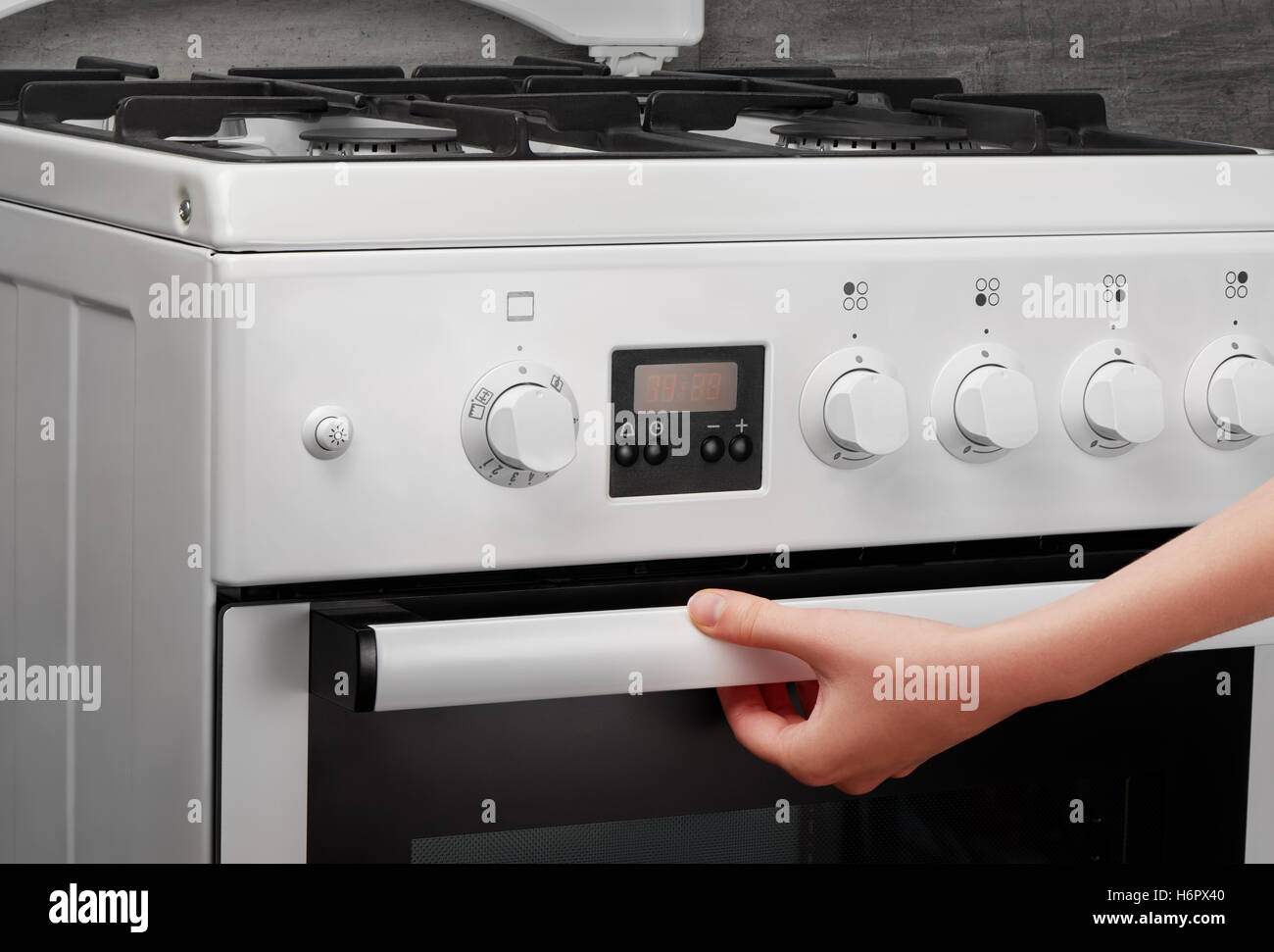 Weibliche Hand öffnen Ofen in weiße Küche Gasherd auf grauem Hintergrund Stockfoto