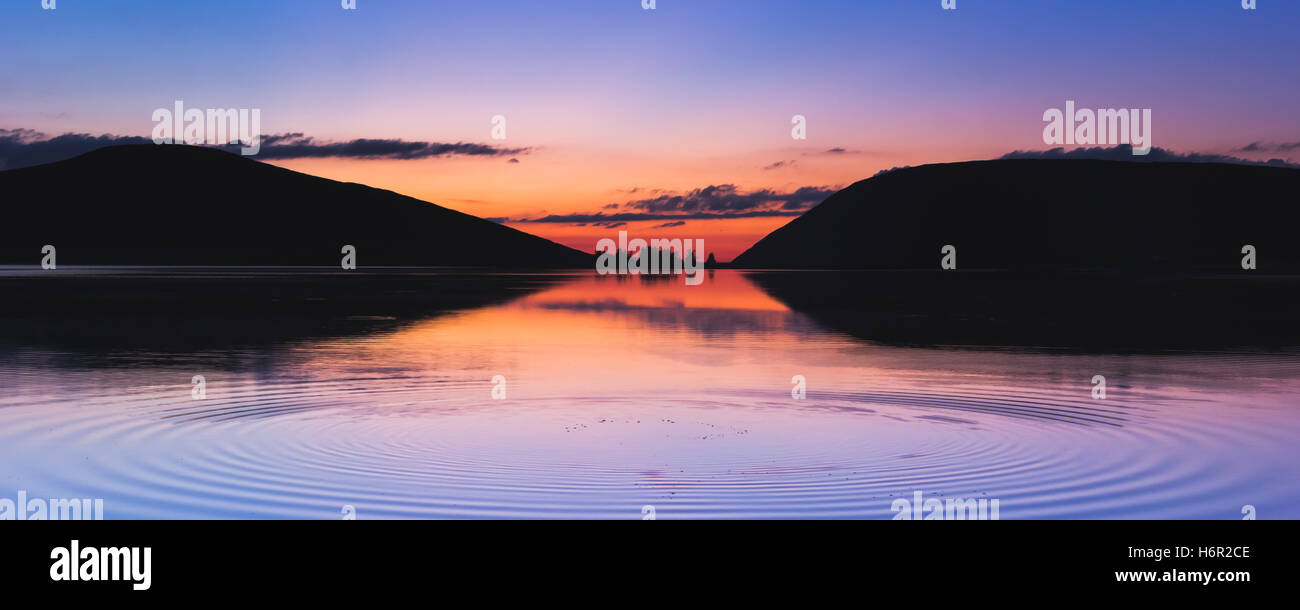 Ein atemberaubender Sonnenuntergang über der Spelga-Stausee in Nordirland mit einem plätschernden, Spiegelung des Himmels auf der Seeoberfläche Stockfoto