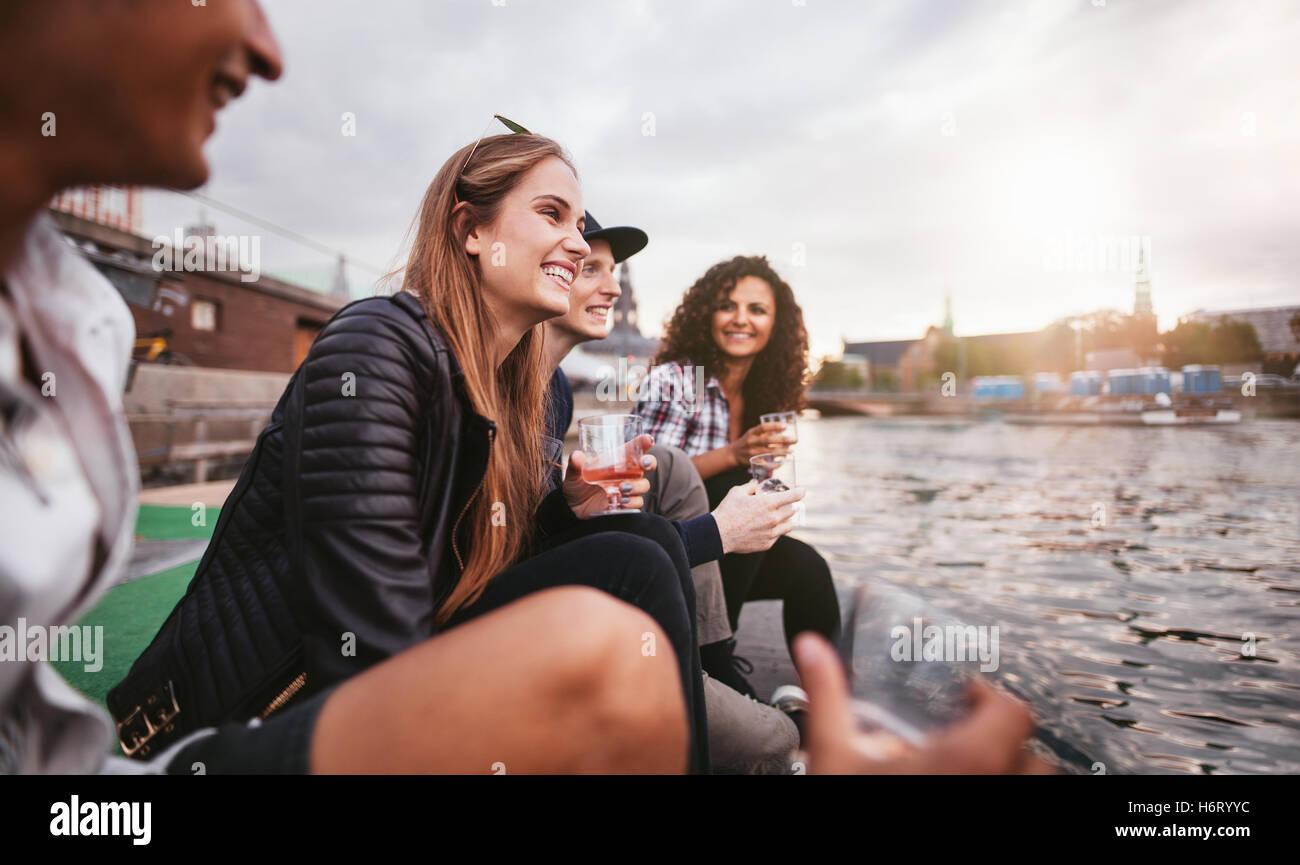 Schuss Gruppe glücklich junger Menschen am See entspannen und Getränke. Teenager Freunde am Steg sitzen und Lächeln auf den Lippen. Stockfoto