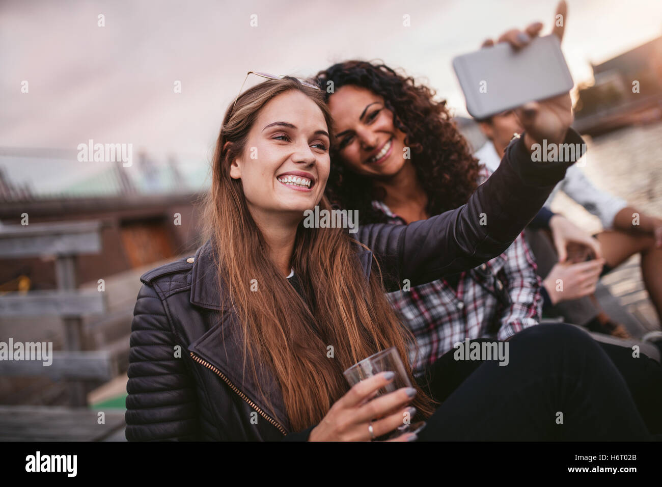 Freunde nehmen ein Selbstporträt mit Smartphone in der Nähe des Sees. Fröhlich zwei junge Frauen, die Selfie mit Handy. Stockfoto