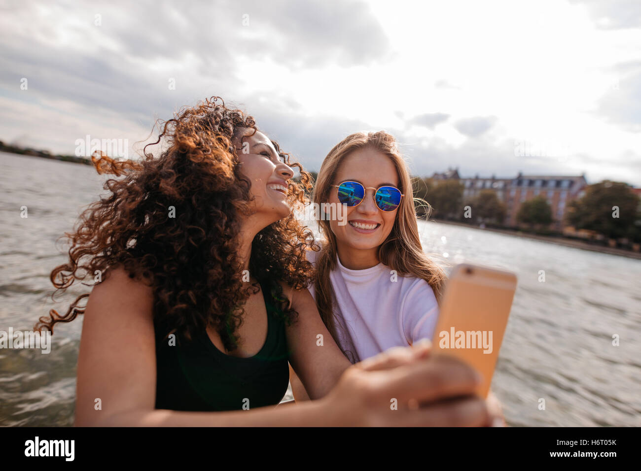 Aufnahme von zwei schönen jungen Frauen, die die Selfie am See. Selbstbildnis mit Smartphone unter Freundinnen. Stockfoto