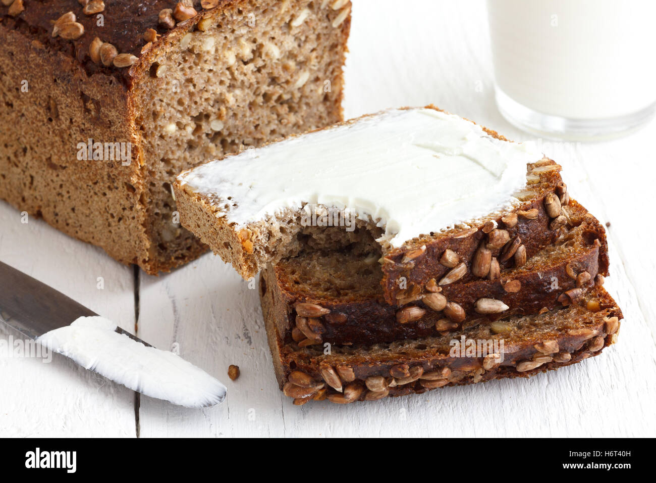 Sonnenblumen-Brot in Scheiben geschnitten, Sahne Schmelzkäse, rustikale Oberfläche, Milch. Stockfoto