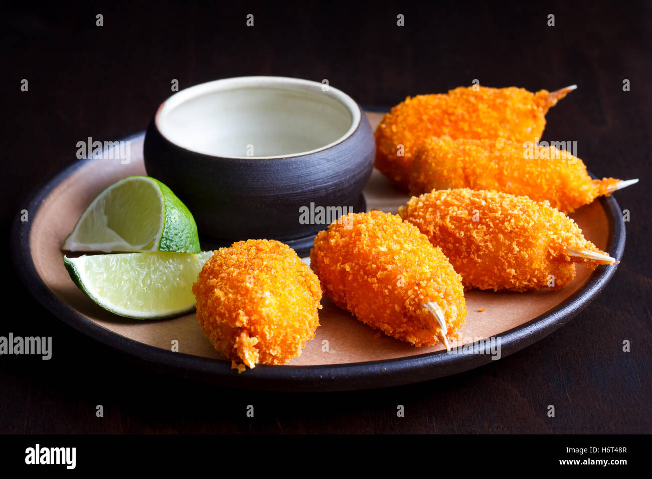 Rustikale Platte gebratene panierte Surimi Scheren mit leeren Dip Schüssel und Zitrone Scheiben isoliert auf schwarz. Stockfoto