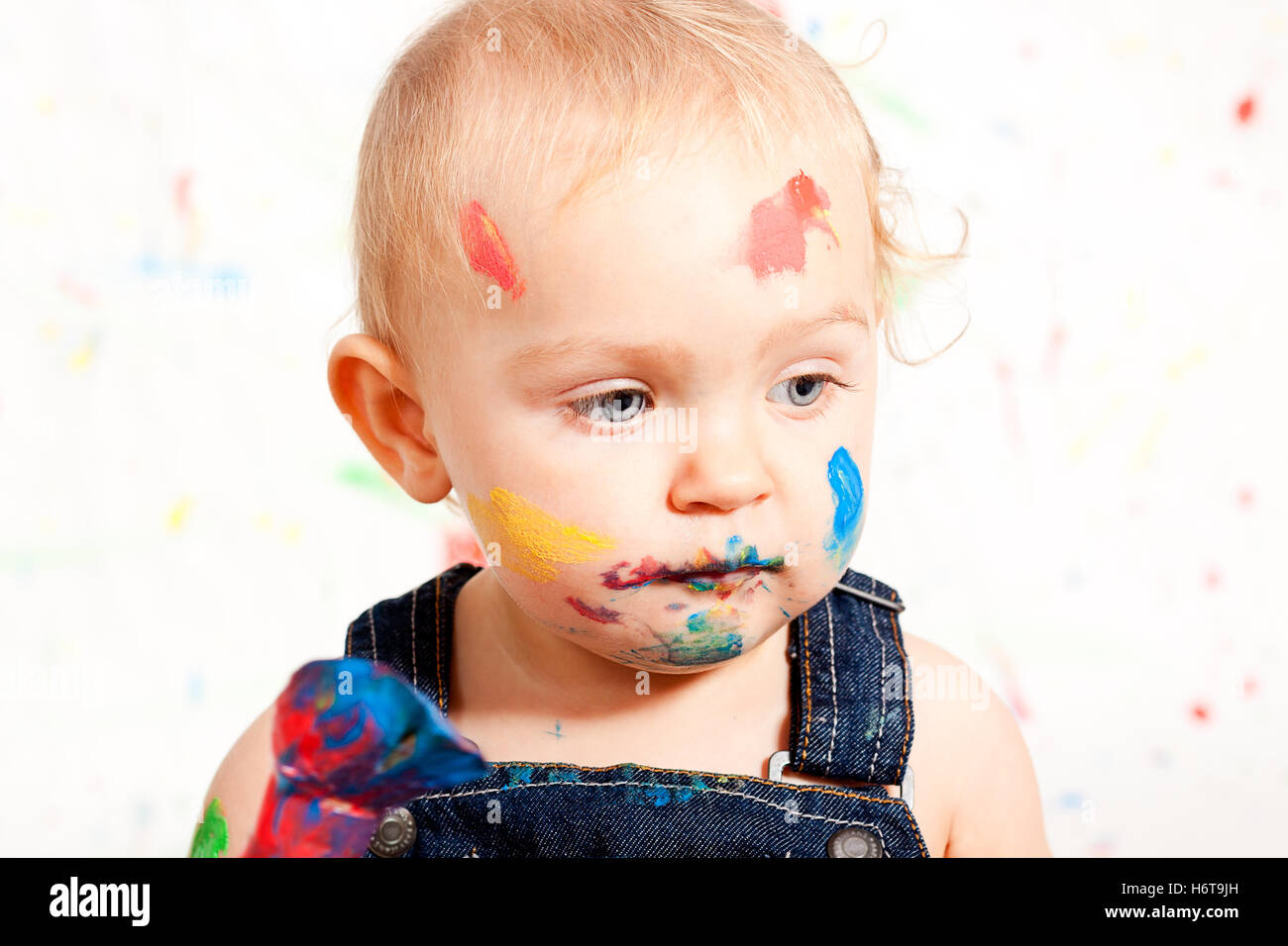 süßes kleines Kind im Overall mit Pinsel und Farben Stockfoto