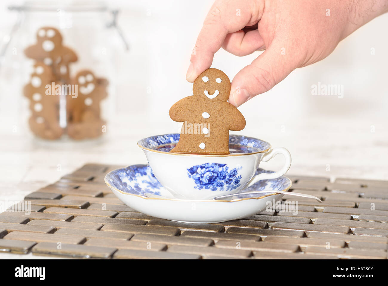 Pfefferkuchen-Mann wird in eine Tasse Tee mit Glas von Cookies im Hintergrund getaucht Stockfoto