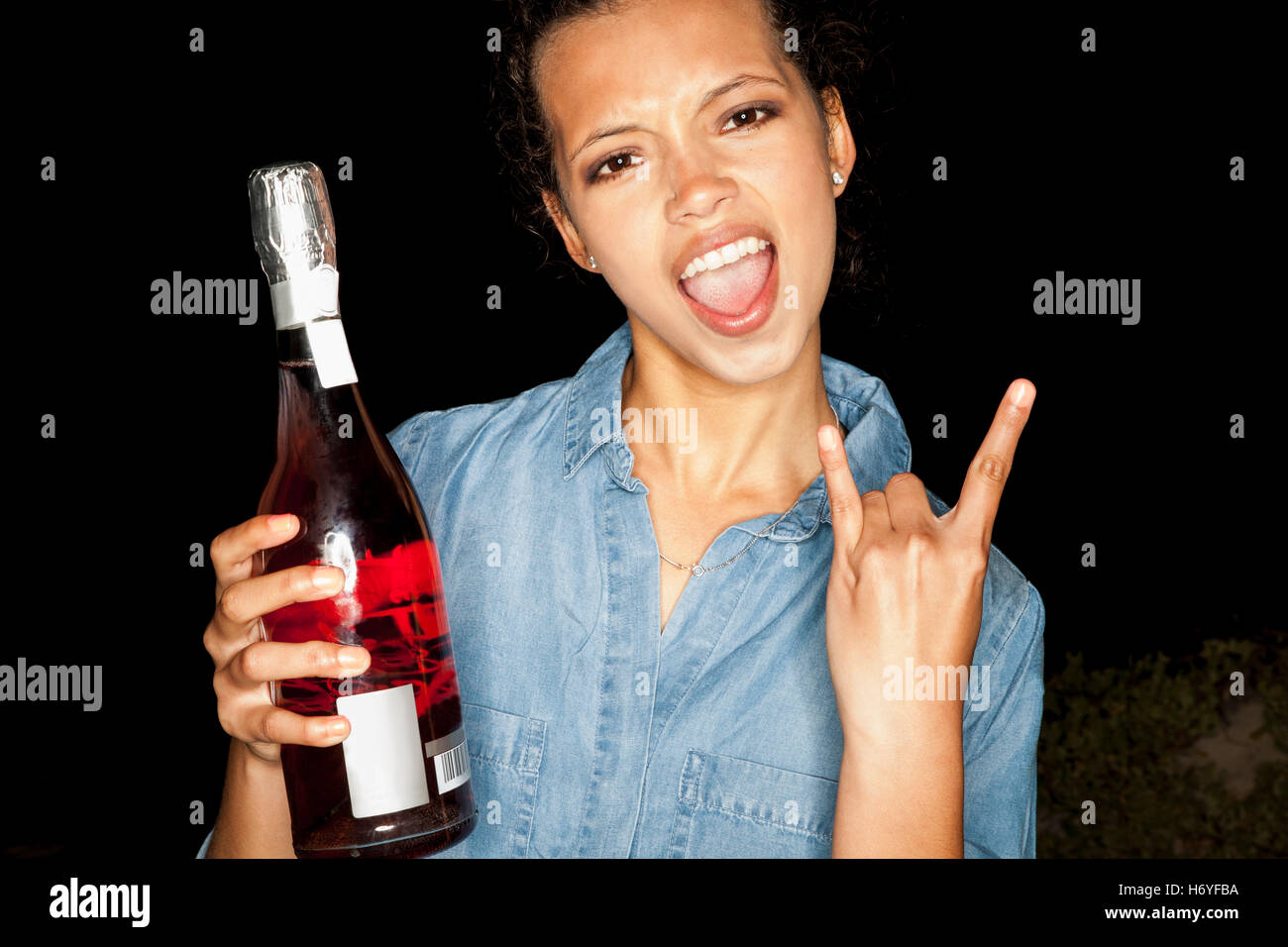 Junge Frau mit Flasche Wein tun Rock Zeichen Blick in die Kamera offen in den Mund genommen Stockfoto