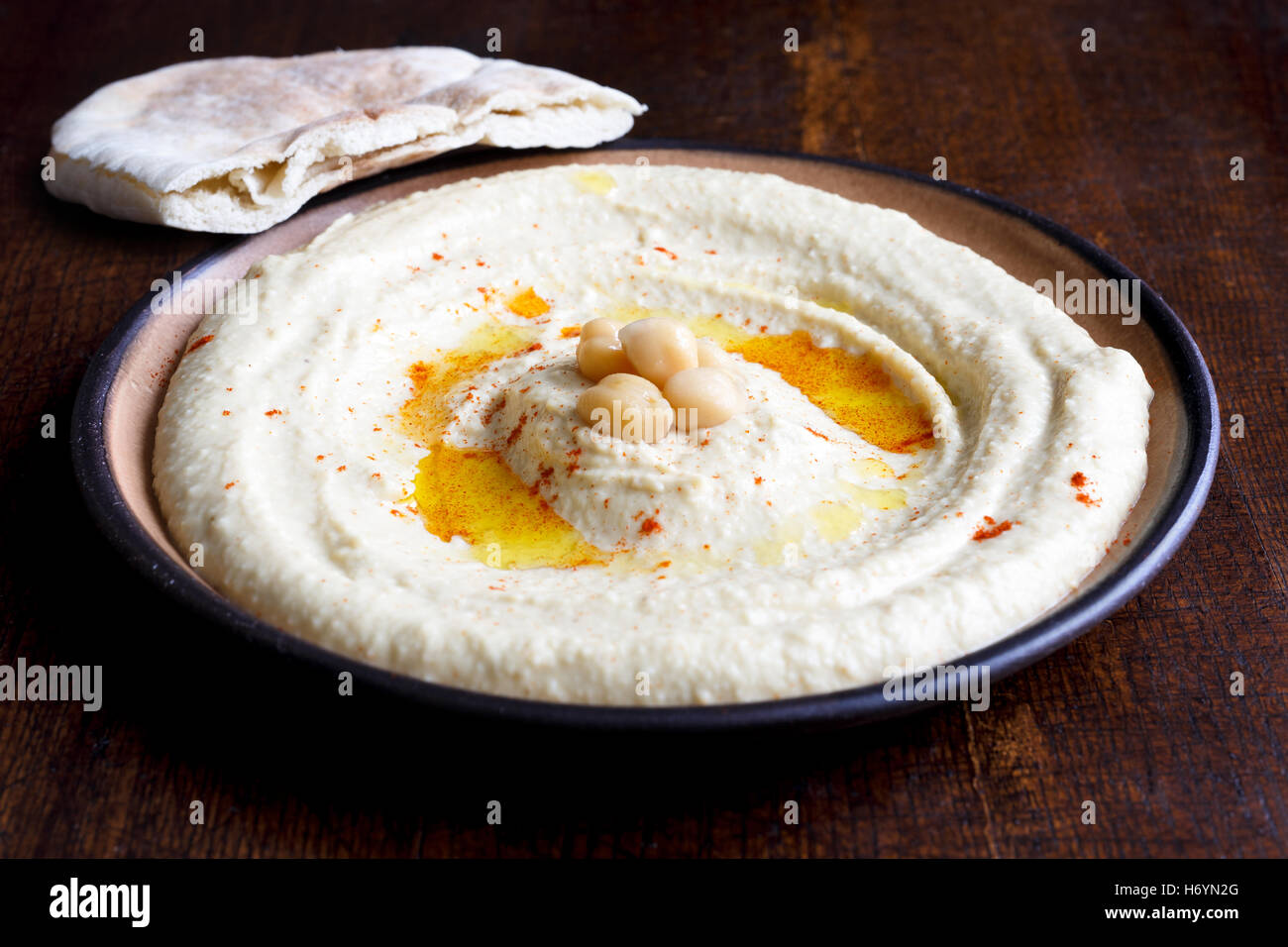 Hummus auf braune Keramik-Platte mit Pita-Brot auf dunklen isoliert. Stockfoto