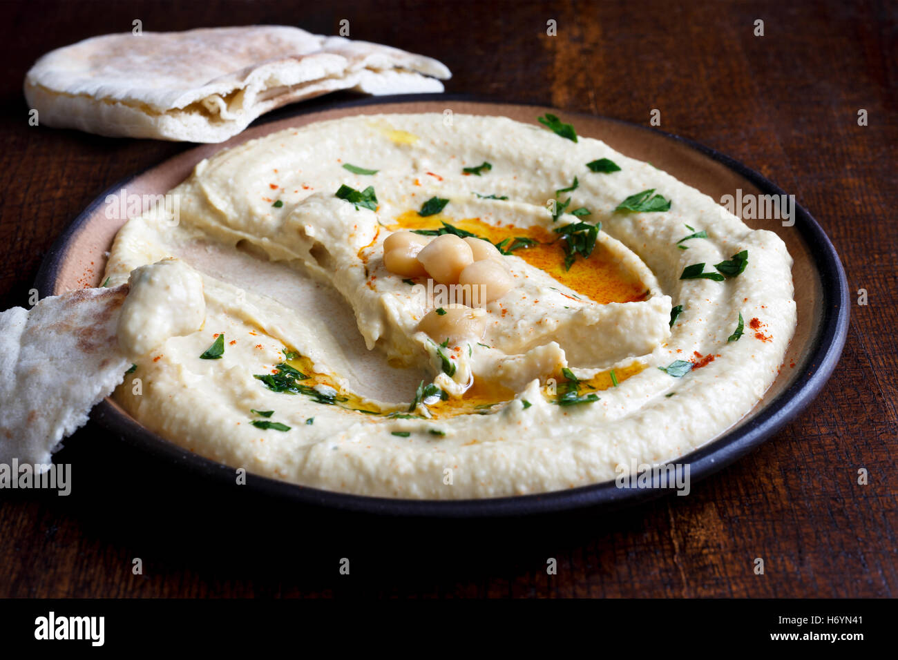 Hummus auf braune Keramik-Platte mit Pita-Brot auf dunklen gegessen. Mit Petersilie garniert. Stockfoto